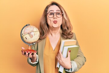 Poster - Middle age caucasian woman holding world ball and books looking at the camera blowing a kiss being lovely and sexy. love expression.