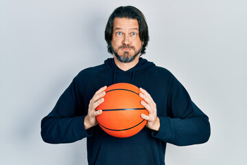 Wall Mural - Middle age caucasian man holding basketball ball puffing cheeks with funny face. mouth inflated with air, catching air.