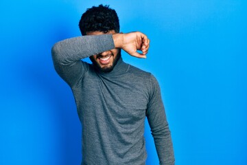 Canvas Print - Arab man with beard wearing turtleneck sweater covering eyes with arm smiling cheerful and funny. blind concept.