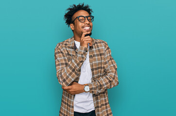 Wall Mural - Young african american man with beard wearing casual clothes and glasses looking confident at the camera smiling with crossed arms and hand raised on chin. thinking positive.