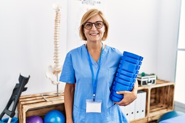 Sticker - Middle age blonde woman wearing physiotherapist uniform holding foam roller at clinic