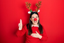 Young Hispanic Woman Wearing Deer Christmas Hat And Red Nose Smiling Swearing With Hand On Chest And Fingers Up, Making A Loyalty Promise Oath