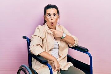 Sticker - Young hispanic woman sitting on wheelchair surprised pointing with finger to the side, open mouth amazed expression.