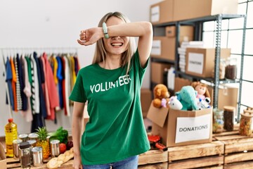 Sticker - Asian young woman wearing volunteer t shirt at donations stand smiling cheerful playing peek a boo with hands showing face. surprised and exited