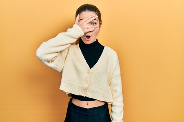 Sticker - Young brunette girl wearing casual yellow jacket peeking in shock covering face and eyes with hand, looking through fingers afraid