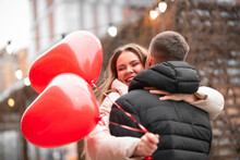Charming Couple Hugging On The Street After A Date. A Young, Beautiful Lady Holds Heart-shaped Balloons In Her Hand And Laughs. Valentine's Day Concept, Gifts, Love
