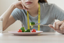 Anorexia, Unhappy Beautiful Asian Young Woman, Girl On Dieting, Hand Holding Fork At Broccoli In Salad Plate, Dislike Or Tired With Eat Fresh Vegetables. Nutrition Of Clean, Healthy Food Good Taste.