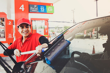 Staff, the smiling male staff, are happy to do the job of cleaning the wiper blades and windshields of customers with pleasure : Excellent customer service work of male staff in a modern gas station.