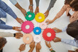 © Studio Romantic - Team of young and senior business people holding and joining colorful gear wheels on office desk as symbol or metaphor for teamwork efficiency and effective collaboration. Top overhead view from above