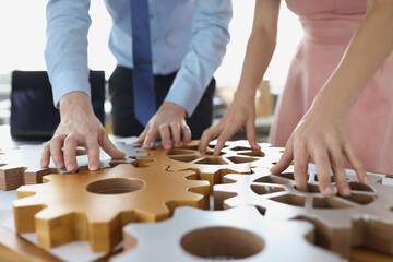 Wall Mural - Business people making whole picture of wooden gears on workplace together in office