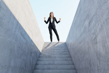 Happy European Businesswoman Celebrating Success On Top Of Abstract Concrete Stairs With Sunlight. Growth And Leadership Concept.