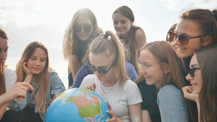 Wall Mural - A group of cheerful girls is exploring the globe of the world in the meadow.