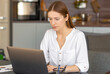 © kucherav - Focused caucasian woman using laptop while sitting in home office, involved online conference, watching training webinar, online education concept