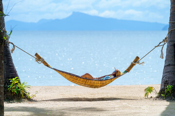 Wall Mural - A young woman relaxing in a hammock on the beach in summer alone on vacation.