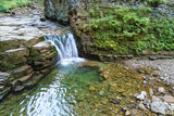 Fototapeta Łazienka - Waterfall on mountain river with white foamy water falling down from rocky formation in summer forest