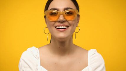 Wall Mural - Positive woman in sunglasses looking at camera isolated on yellow.