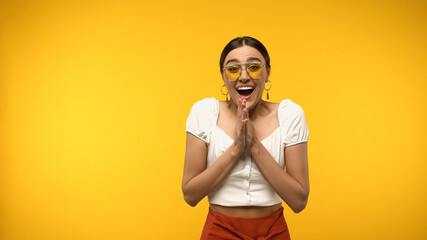Wall Mural - Excited woman in blouse and sunglasses looking at camera isolated on yellow.