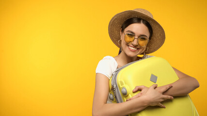Wall Mural - Happy woman in straw hat hugging suitcase isolated on yellow.