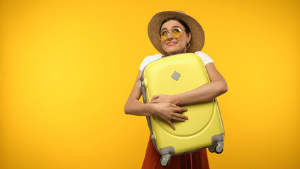 Wall Mural - Smiling tourist in sunglasses holding baggage isolated on yellow.