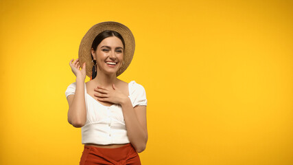 Wall Mural - Smiling model in blouse and straw hat looking at camera isolated on yellow.