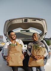 Diverse couple with grocery at car trunk