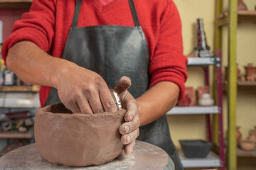 View of hands of a potter making and molding with tool a ceramic bowl in his workshop