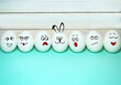 © Alleksa - A line of eggs with different facial expressions and an Easter bunny on a turquoise and wooden background. Funny Easter eggs.