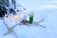 Wiccan Altar For Imbolc Sabbath, Pagan Holiday Ritual. Brigid's Cross Of Straw, Candles, Snowdrops, Toy Sheep On Snow, Winter Forest Natural Background. Symbol Of Imbolc Holiday, Spring Equinox.