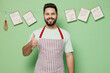 Young satisfied happy smiling male chef confectioner baker man 20s in striped apron showing thumb up like gesture isolated on plain pastel light green background studio portrait. Cooking food concept.