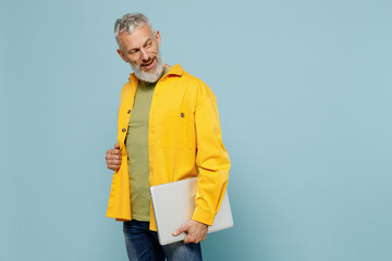 Sticker - Elderly side view happy gray-haired mustache bearded man 50s in yellow shirt hold closed laptop pc computer look aside on workspace copy space isolated on plain pastel light blue background studio