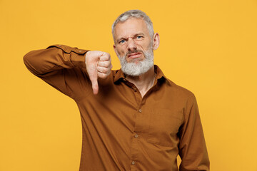 Irritated upset nervous displeased elderly gray-haired bearded man 40s years old wear brown shirt looking camera showing thumb down dislike gesture isolated on plain yellow background studio portrait