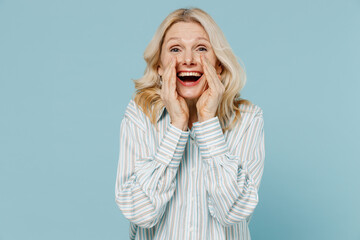 Wall Mural - Elderly promoter woman 50s wear striped shirt scream hot news about sales discount with hands near mouth isolated on plain pastel light blue color background studio portrait. People lifestyle concept.