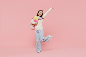 Wall Mural - Full body smiling happy cheerful teen student girl of Asian ethnicity in sweater hold backpack book stretch hand isolated on pastel plain light pink background Education in university college concept.