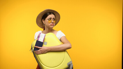 Wall Mural - Dissatisfied tourist in sunglasses and straw hat holding suitcase and passport isolated on yellow.