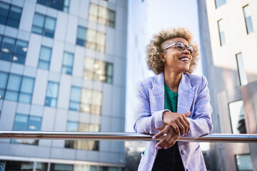 Young African American business woman in trendy outfit and eyeglasses standing on corporate urban district. Creative female professional in the city