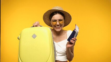 Wall Mural - Smiling tourist in straw hat holding baggage and passport isolated on yellow.