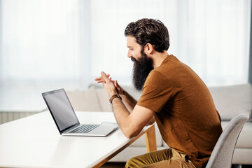 A bearded entrepreneur looking at the laptop while working remotely from his home.