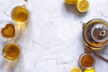 Teapot and cups of tea on a light marble table with lemons and honey, top view. The best remedy in the cold season.