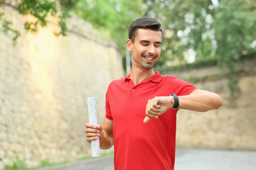 Wall Mural - Young male tourist with smartwatch and map outdoors