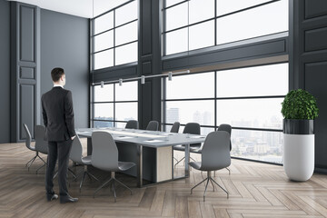 Poster - Businessman standing in modern wooden and concrete meeting room interior with panoramic city view, furniture and daylight. Success and workplace concept.