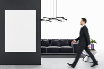 Canvas Print - Businessman walking in modern bright white living room interior with empty mock up poster on wall, couch, table, concrete flooring and decorative items. Home designs concept.