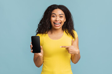 Wall Mural - Overjoyed african american lady pointing at modern smartphone empty blank screen over blue background