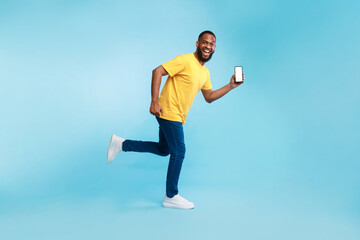 Poster - Young Afro guy with blank smartphone running on blue background, demonstrating mockup for mobile app, website