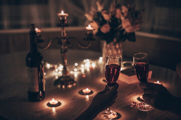 Hands man and woman holding glasses of wine having romantic candlelight dinner at table at home. Hands man and woman holding glass of wine. Concept of Valentine's day or Candlelight date at night.