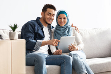 Wall Mural - Beautiful middle-eastern couple sitting on couch with pad