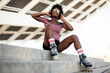Beautiful African woman with roller skates. Urban sexy girl sitting on the stairs listening the music