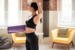 © WellStock - Attractive woman with slender body holding yoga mat and looking aside. Fitness lady with dark hair taking break during domestic workout.