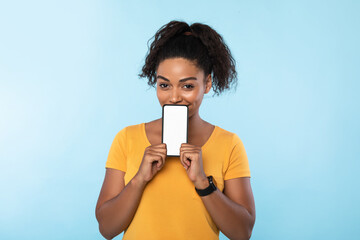 Poster - Afro woman holding cellphone with mockup space next to her face over blue background. New awesome mobile app, website