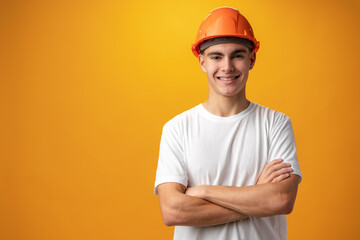 Confident smiling teen boy wearing orange hard hat against yellow background