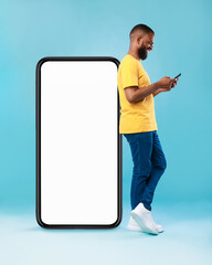 Poster - Afro guy using cellphone while leaning on giant mobile phone with empty screen, mockup for app or website, space for ad